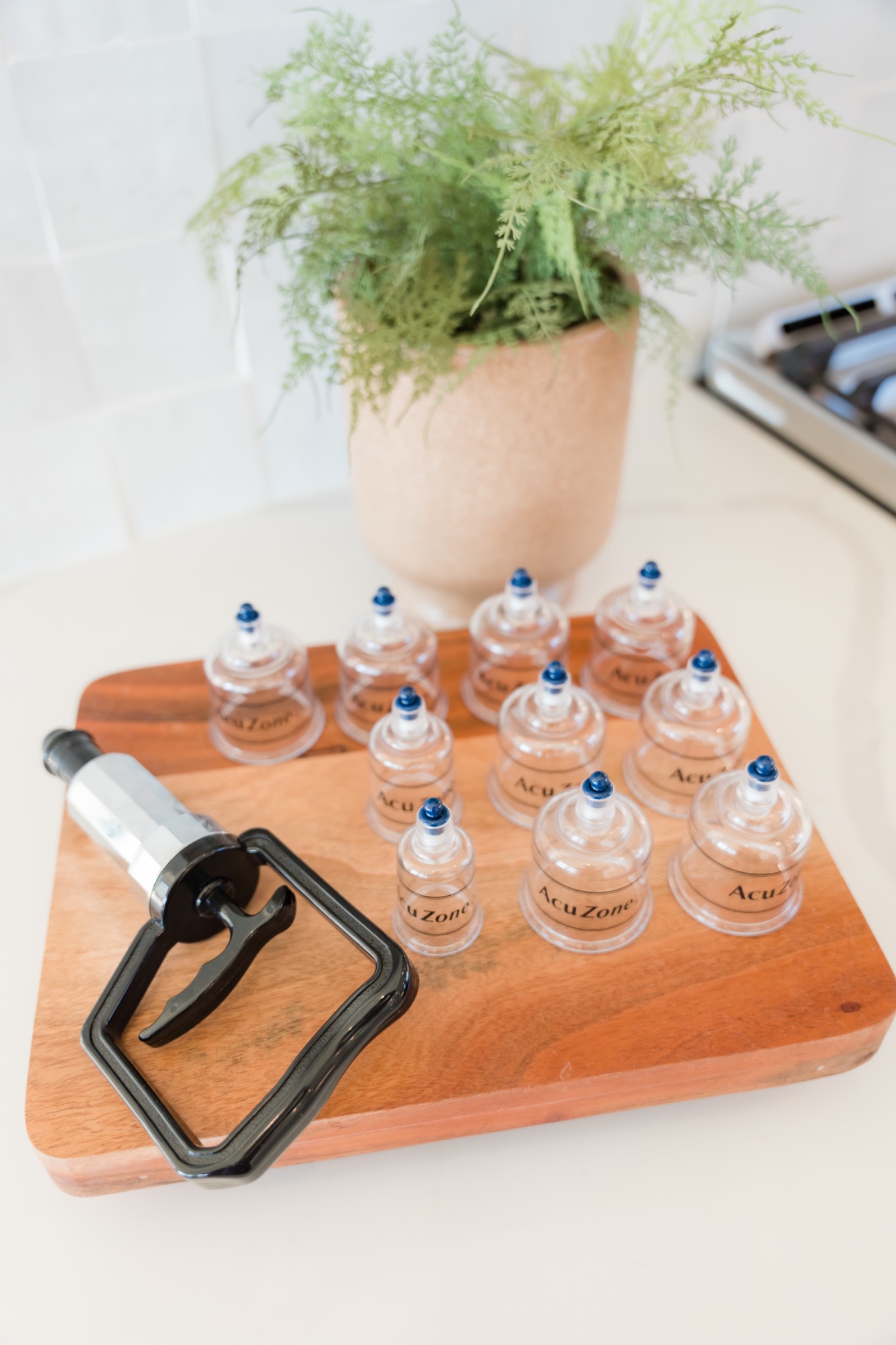 Cupping cups and a hand pump arranged on a wooden tray beside a green plant